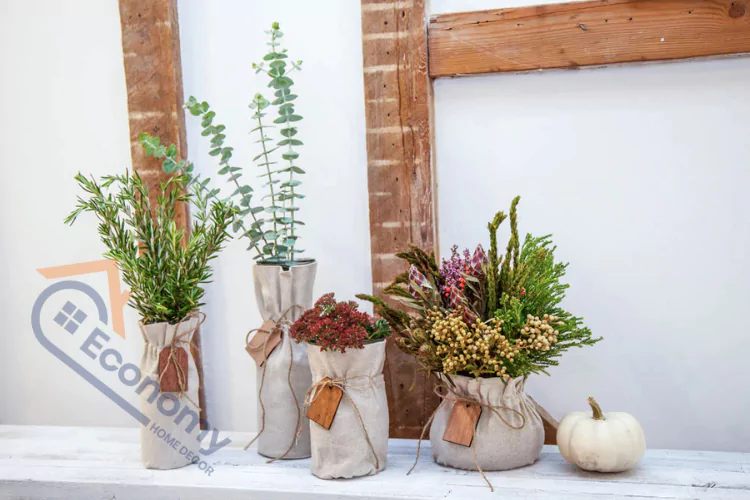 Fall-themed home decor featuring potted plants and dried flowers in rustic fabric-wrapped vases, with a miniature white pumpkin on a white shelf.