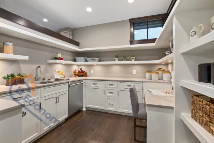 Modern pantry design with white shaker cabinets, open shelving filled with decorative containers and plants, a small desk area with a chair, and recessed lighting.