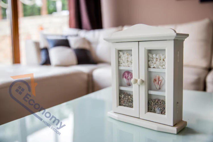 An image demonstrating "Seashell Decorating Ideas," showcasing a decorative display cabinet holding a collection of natural seashells, with a neutral-colored couch in the background.