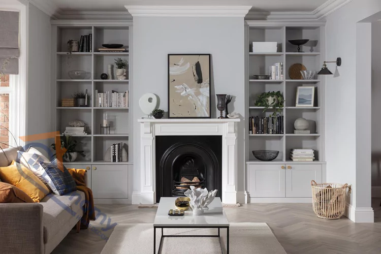 A traditional living room with a fireplace, featuring built-in gray alcove bookcases on either side of the mantel, showcasing books and decorative objects.