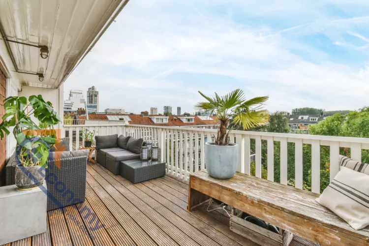 A spacious urban balcony with a modern gray outdoor sofa, a white railing, and a slatted wood floor.
