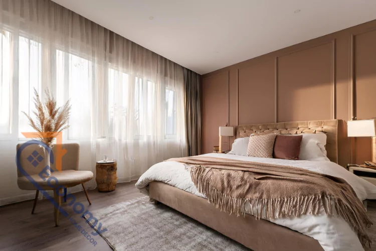 A warm and inviting bedroom with beige-toned decor, featuring a plush bed with a velvet headboard and a variety of pillows in complementary shades.