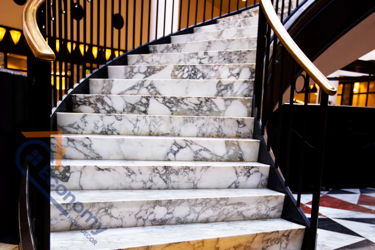 A modern interior with a striking curved staircase, featuring white marble steps with gray veining and a black railing with a golden brass handrail.