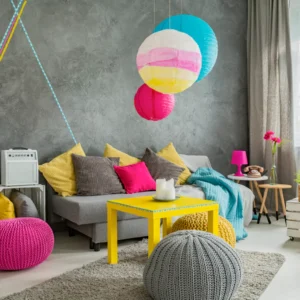 Vibrant and eclectic living room with a grey textured wall, colorful paper lanterns, yellow coffee table, and pink and grey poufs.