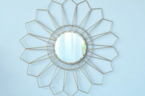Geometric gold sunburst wall mirror with a round central mirror on a light blue wall.