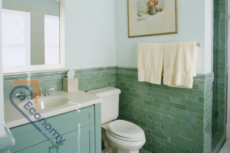 A traditional bathroom with mint green tile on the lower half of the walls and around the shower area, and a light blue paint color above.