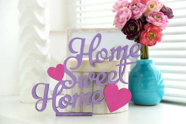 "Home Sweet Home" decorative wood sign with purple lettering and pink hearts on a white table.