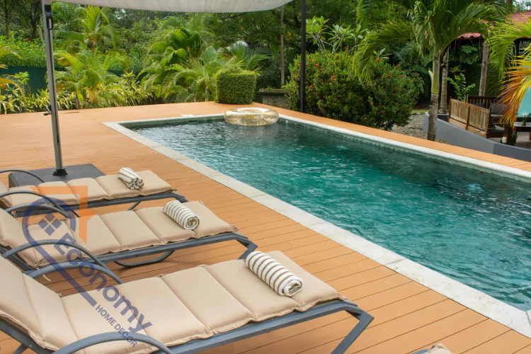 A relaxing tropical outdoor space with a swimming pool and a light brown pool deck furnished with chaise lounges and a white patio umbrella.