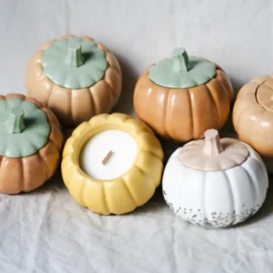 Rustic chic autumn decor featuring pumpkin-shaped ceramic containers and a candle on a linen cloth with birch wood.