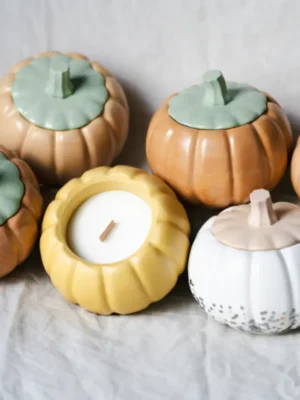Rustic chic autumn decor featuring pumpkin-shaped ceramic containers and a candle on a linen cloth with birch wood.