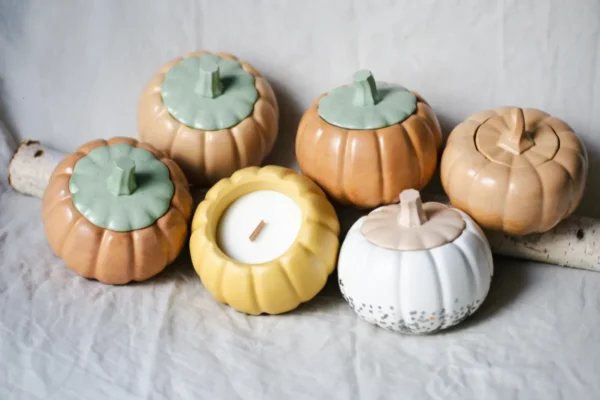 Rustic chic autumn decor featuring pumpkin-shaped ceramic containers and a candle on a linen cloth with birch wood.