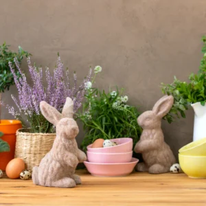 Spring and Easter table decor with two flocked bunny figurines, fresh eggs, and potted plants on a wooden surface.