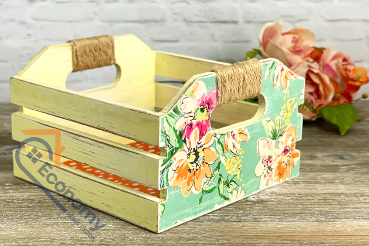 A decorative wooden crate painted light yellow and accented with floral patterned fabric, with handles wrapped in natural twine.