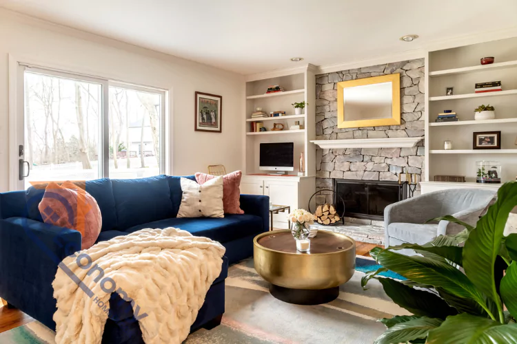 A cozy family room with a large navy blue velvet sectional sofa and a stone-faced fireplace flanked by white built-in bookshelves.