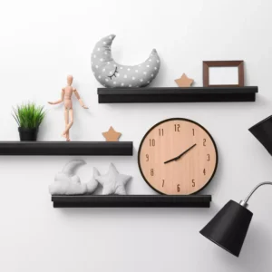 Three black floating shelves decorated with a large wooden clock, plush moon and star pillows, a mannequin, and a small picture frame.