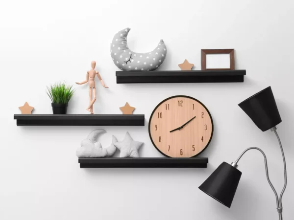 Three black floating shelves decorated with a large wooden clock, plush moon and star pillows, a mannequin, and a small picture frame.