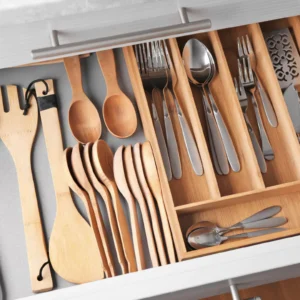 Open kitchen drawer with a bamboo wood organizer filled with wooden spatulas, spoons, and stainless steel flatware.