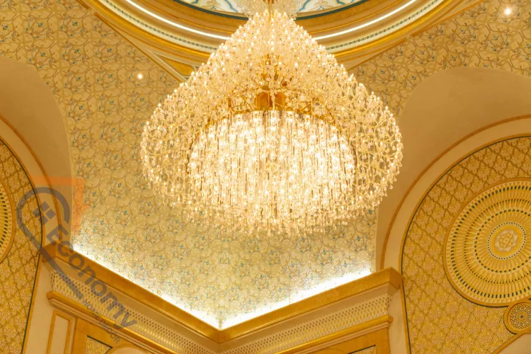 A spectacular, dome-shaped crystal chandelier hanging from a luxurious, gold-patterned vaulted ceiling.