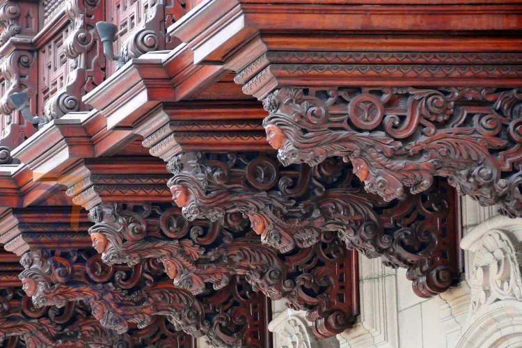 A close-up of intricate, carved wooden corbels on a building exterior, featuring detailed scrolling and stylized human faces.