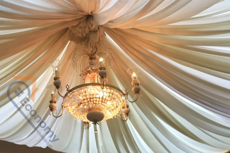 A large, antique crystal chandelier hanging from a central hook on the ceiling, surrounded by dramatic fabric draping.