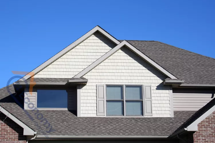 A close-up of a house's upper exterior highlighting the dormer's different siding and the composition shingle roof.