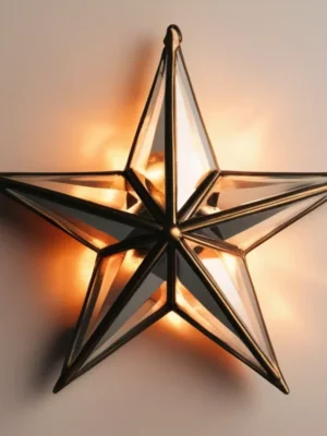 Antiqued Brass and Glass Celestial Star Sconce Illuminated 3D star wall sconce with antiqued brass metal frame and beveled glass panels, casting a warm orange glow.