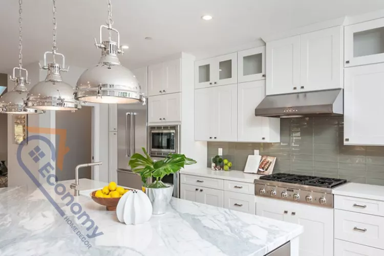 Modern kitchen with white shaker cabinets, a large marble-top island, a stainless steel commercial range under a hood, gray subway tile backsplash, and three large polished chrome pendant light fixtures hanging over the island.