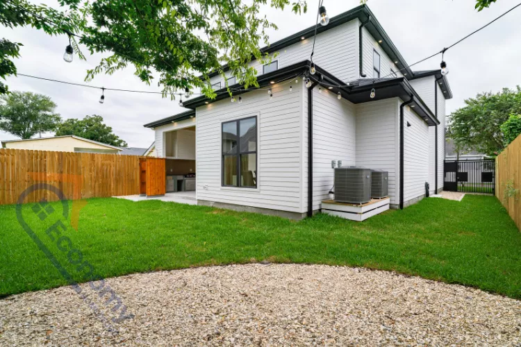 DIY backyard upgrade showing a fresh lawn, a simple gravel patio area, a wooden fence, and string lighting installed on a modern home exterior.