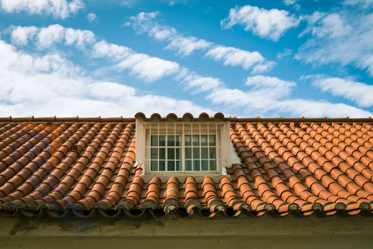 Close-up of a house roof covered in classic orange terracotta tiles with a small white-framed window.