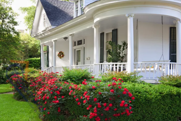 A cozy small porch decorating idea featuring a plush gray outdoor sofa tucked into a white-columned corner.