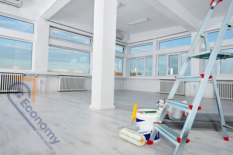 Interior of a large, empty room with painting supplies and an aluminum ladder, indicating preparation for a remodel, painting, or thorough spring cleaning.