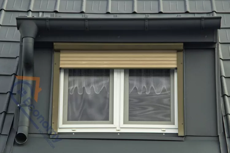A modern gray metal dormer window featuring a functional beige roller shutter and simple white frames.