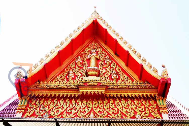 A stunningly intricate red and gold gable decoration idea featuring traditional Thai Buddhist figures and floral motifs.