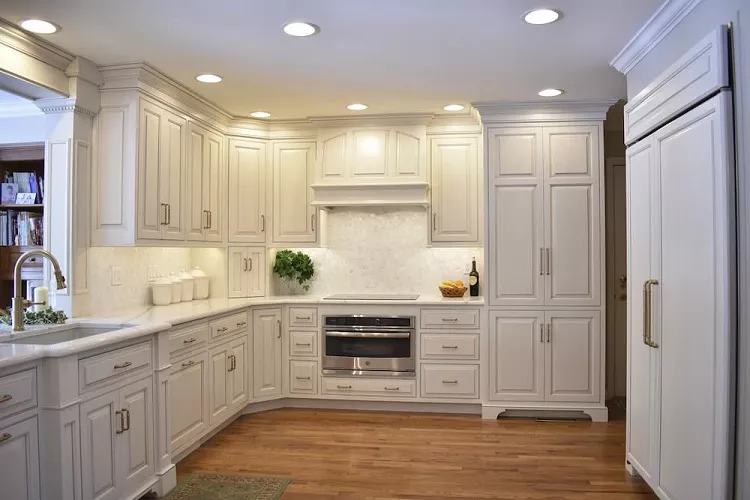 Elegant white kitchen with custom cabinetry, built-in oven, recessed ceiling lights, marble backsplash, and warm hardwood flooring