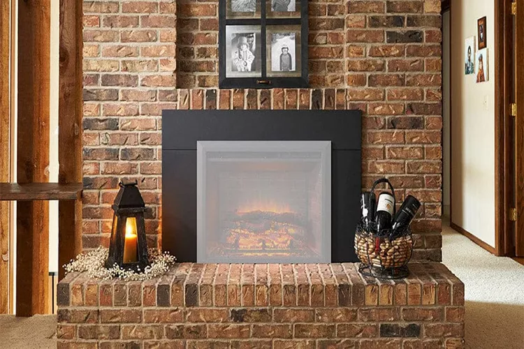 A close-up shot of a rustic, red-brick fireplace hearth featuring a black-framed electric insert, a wicker basket of wine bottles, and a lantern with a lit candle, surrounded by baby's breath.