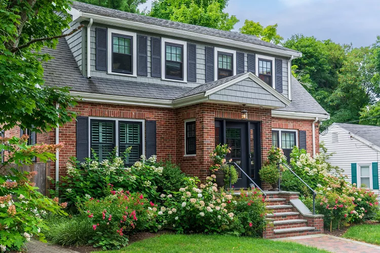 Traditional brick house exterior with black shutters, landscaped front garden, and welcoming front porch surrounded by lush greenery
