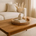 Styled coffee table with rattan tray, stacked books, ceramic vase and candle in a bright living room